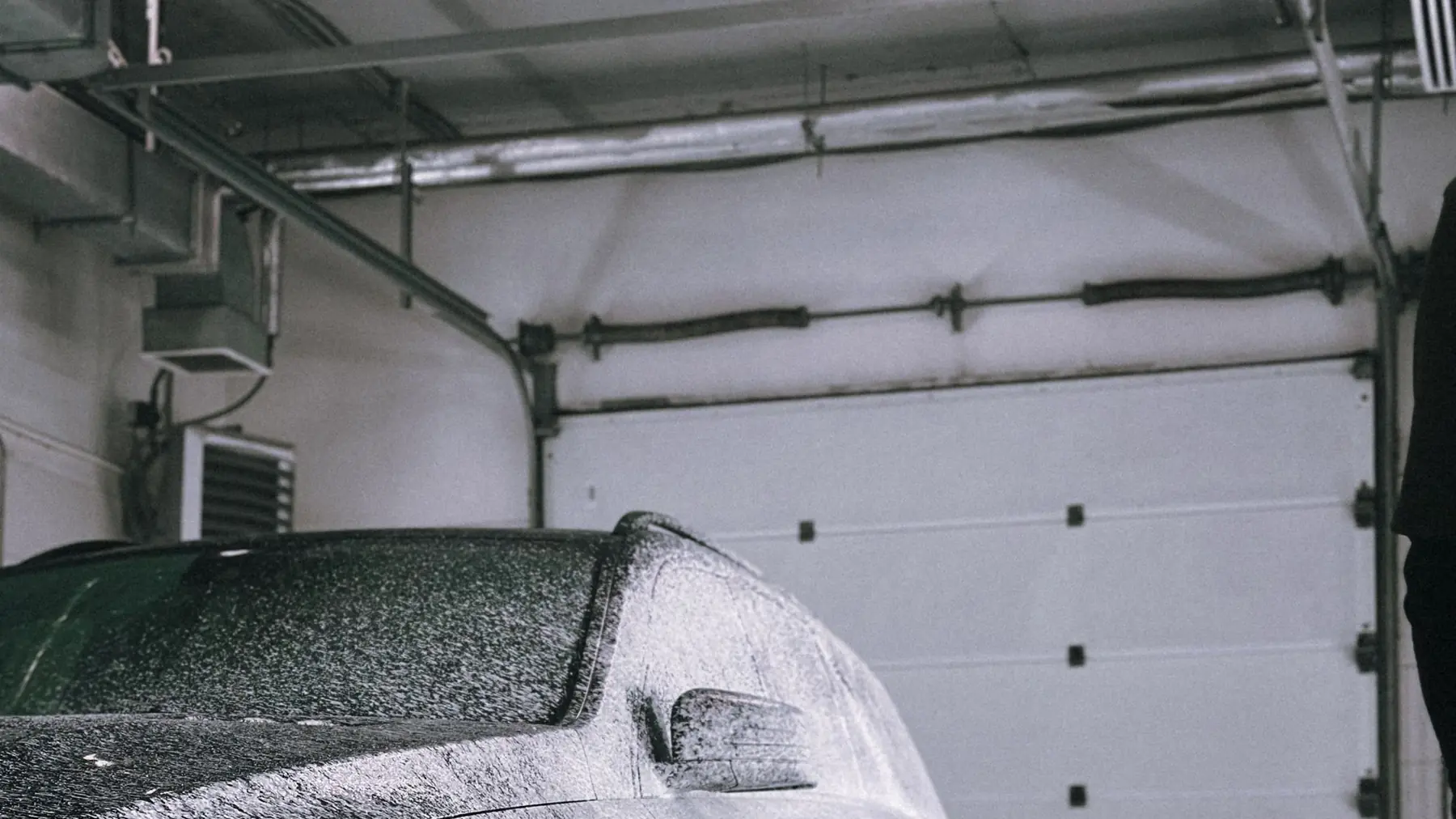 A car covered in thick wash foam inside a lit garage