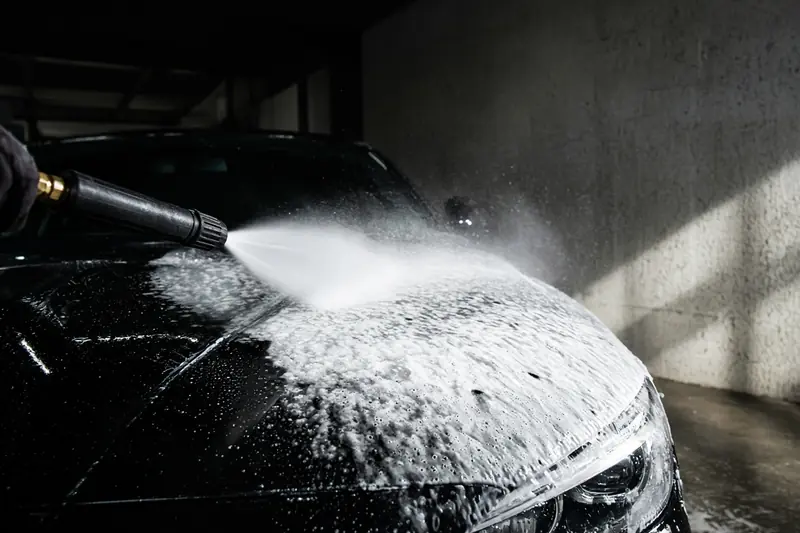 A foam cannon laying snow foam on a black car